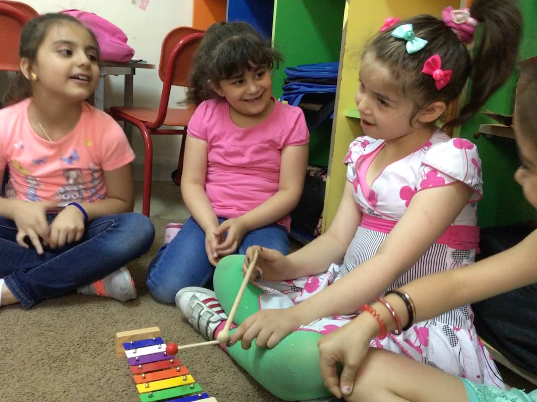 Girls sat on the floor playing a xylophone smiling at each other.